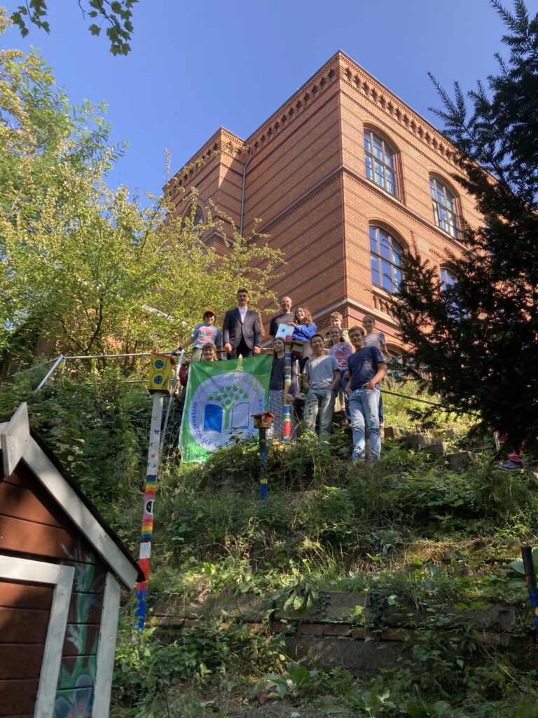 Schülergruppe mit Schulleiter und Lehrer im Schulgarten mit Urkunde